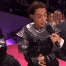 a man in armor is talking into a microphone while sitting on a pink couch