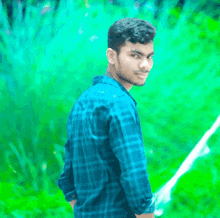 a young man in a blue plaid shirt is standing in front of a green background