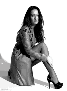a woman in a trench coat and high heels is kneeling down in a black and white photo
