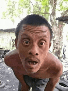 a shirtless man with a beard is making a funny face while standing in front of a pile of tires .