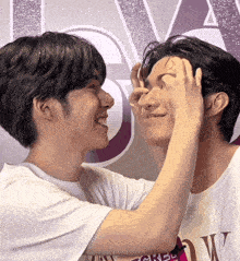 two men are touching each other 's faces in front of a sign that says ' a '