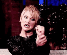a woman in a black dress is making a funny face with her fist in the air .