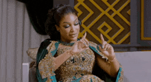 a woman in a gold and green dress is sitting on a couch and making a gesture with her hands .