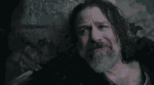 a man with long hair and a beard looks to his left