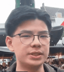 a young man wearing glasses is standing in front of a crowd of people