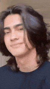 a young man with long black hair is smiling and looking at the camera .