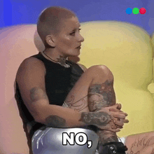 a woman with a shaved head sits on a couch and says " no "