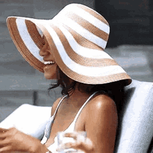 a woman wearing a striped hat is sitting in a chair drinking a glass of water .