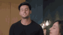 a man in a black shirt is sitting next to a woman with his eyes closed