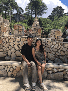 a man and a woman sit on a rock wall