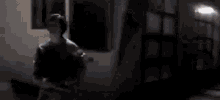 a person is standing in front of a window in a dark room with a light on .