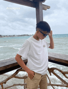 a young man stands on a balcony overlooking the ocean with the words aray koooo on the bottom left