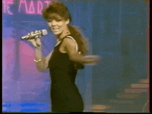 a woman is singing into a microphone in front of a neon sign that says the martins