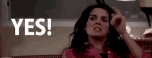 a woman is sitting on a couch making a funny face and pointing at the camera with the word yes .