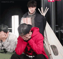 a man in a red hoodie is covering his face while two other men look on