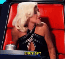 a woman in a black dress is sitting in a red chair and says shut up