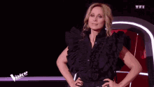 a woman in a black ruffled shirt is standing with her hands on her hips in front of a tfi logo .
