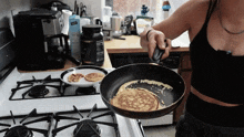 a woman is cooking pancakes on a stove with a box of kirkland protein in the background