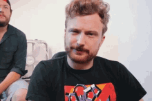a man with a beard is wearing a black shirt with a red graphic on the front