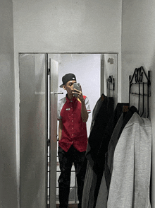 a man in a red shirt is taking a picture of himself in the mirror