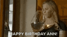 a woman is drinking a large glass of wine and saying `` happy birthday ann '' .