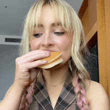 a woman with blonde hair and pink braids is eating a sandwich