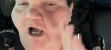 a close up of a woman 's face with her mouth open and a hand behind her ear .
