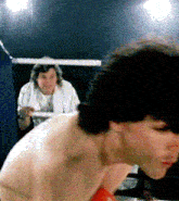 a man in a white shirt is standing in a boxing ring with another man