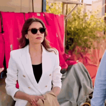 a woman wearing sunglasses and a white jacket is sitting in front of a row of red jackets .