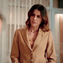 a woman in a tan suit is standing in front of a fence .