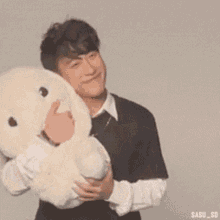 a man is holding a white teddy bear in his arms and smiling .