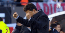 a man in a suit is covering his face with his fist while standing in front of a crowd .