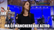 a woman in a black shirt stands in front of a blue wall with the words ma ci mancherebbe altro written on it