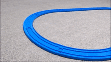 a toy train is going around a blue track on a carpeted floor