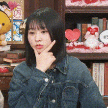 a woman in a denim jacket is sitting in front of a bookshelf and making a funny face .