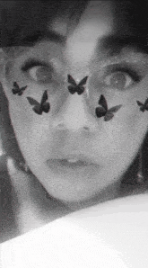 a black and white photo of a woman 's face with butterflies on her face .