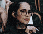 a woman wearing glasses and a black shirt is holding a pen .