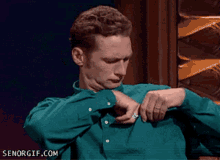a man in a green shirt is looking at his watch and senorgif.com is in the corner