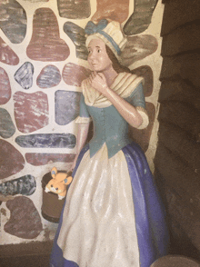 a statue of a woman in a blue and white dress is holding a stuffed animal