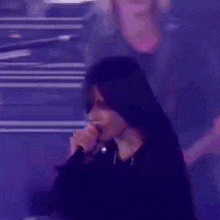 a woman is singing into a microphone on stage in a dark room .
