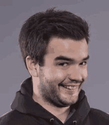 a man with a beard wearing a black hoodie is smiling .