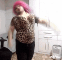 a woman with pink hair and a leopard print shirt is dancing in a kitchen .