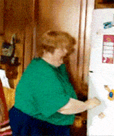 a woman in a green shirt opens a refrigerator door