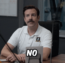 a man sitting at a desk with a laptop that says no