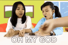two young girls are sitting at a table with a plate of food and the words oh my god written on the bottom