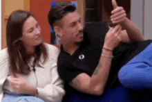 a man and a woman are sitting next to each other on a couch . the man is giving a thumbs up .