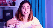 a woman in a white sweater is making a funny face while standing in front of a blue curtain .