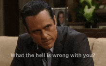 a man in a suit is sitting on a couch with the words what the hell is wrong with you below him