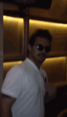 a man wearing sunglasses and a white shirt stands in front of a wall