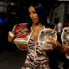 a woman in a camo outfit is holding two wrestling belts